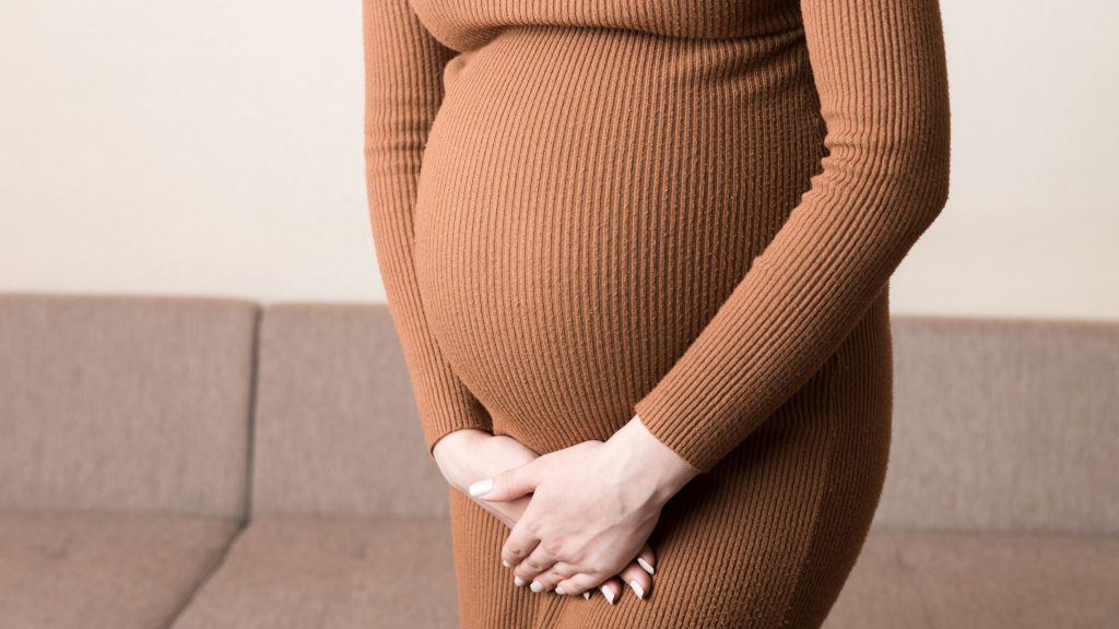 Pregnant woman holding her lower abdomen, illustrating how pregnancy can cause stress incontinence.