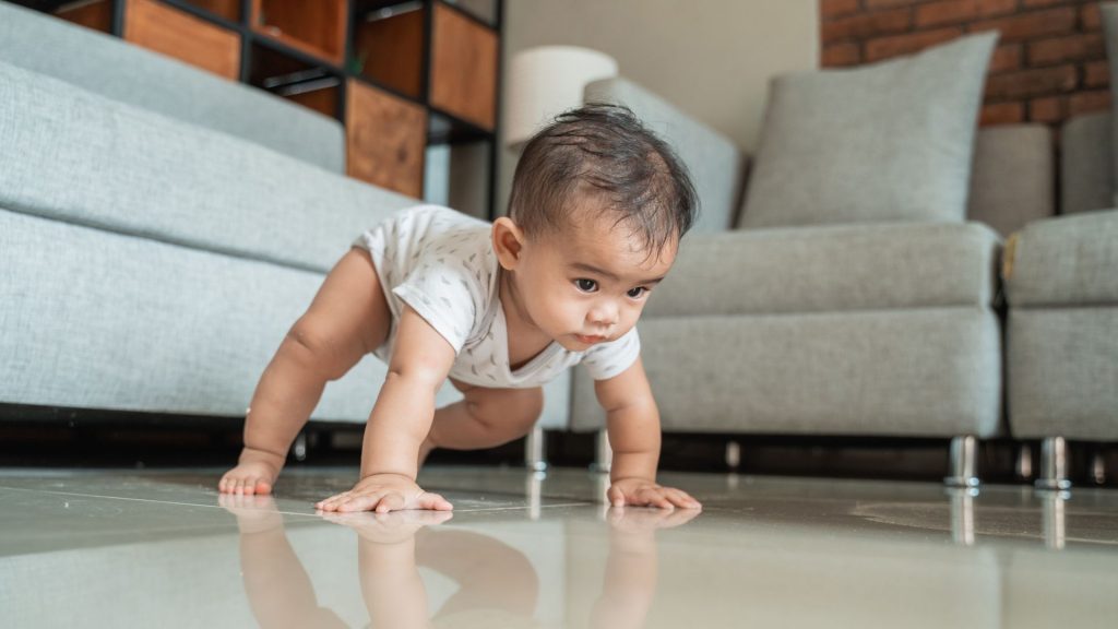A baby crawling in a high-bear position on the floor, practising early motor development and core strength.