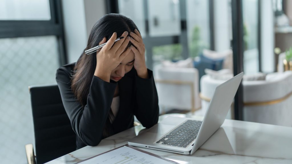 Woman sitting at her desk with her head in her hands, feeling stressed and anxious, illustrating how urinary incontinence can affect confidence, focus, and emotional well-being among working adults in Singapore.