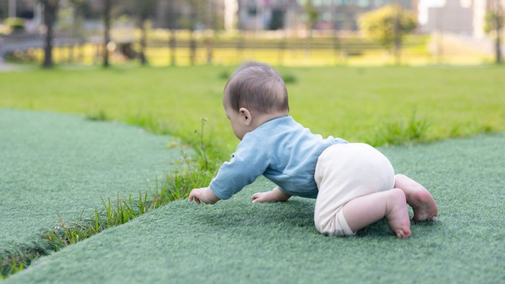 A baby crawling on grass outdoors, developing strength, coordination, and sensory exploration.