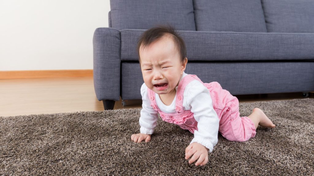 A baby crying while attempting to crawl, a possible sign of discomfort or difficulty with motor milestones.