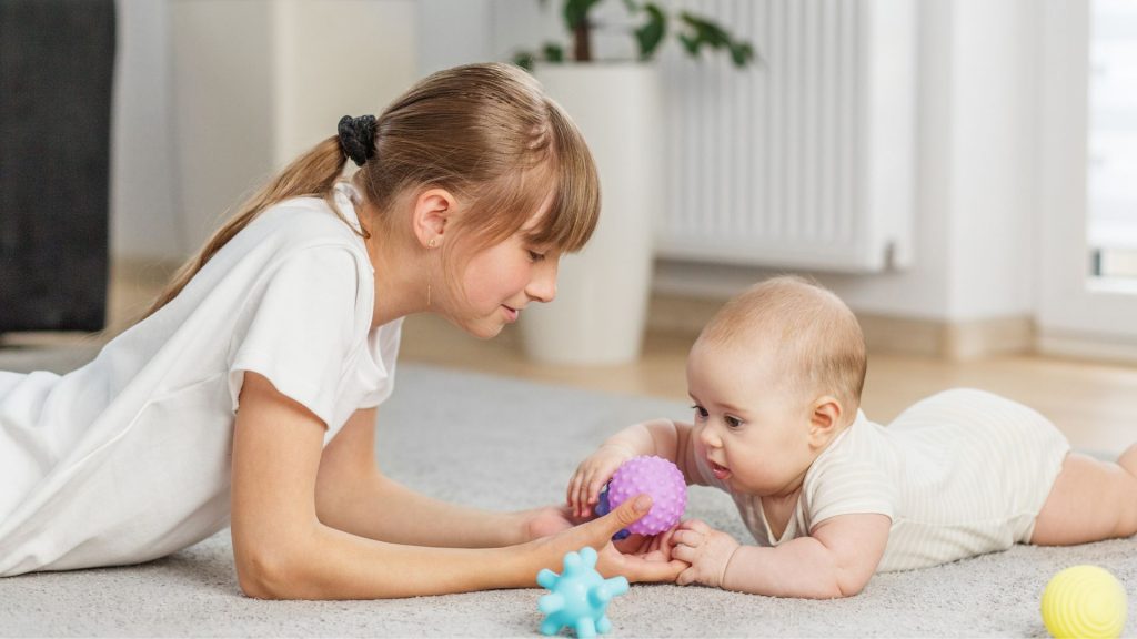 A baby practising tummy time with an older sibling, helping build neck, shoulder, and core strength.