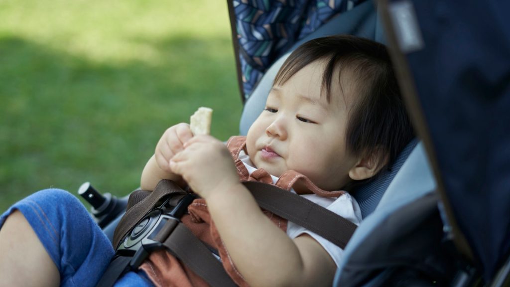 A baby sitting in a stroller holding a snack, a reminder to balance equipment time with active floor play.