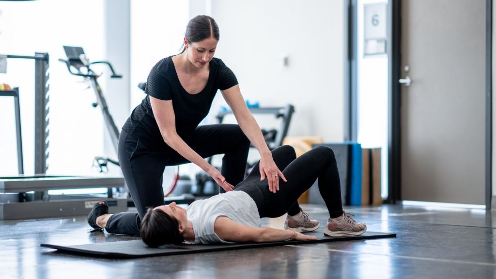 Physiotherapist assisting a woman performing pelvic floor and core strengthening exercises on a mat, demonstrating a key component of urine incontinence treatment for adults in Singapore.
