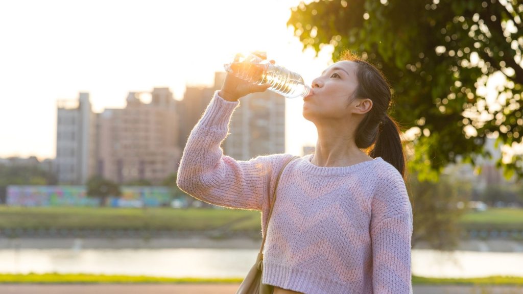 Woman drinking water outdoors in Singapore, demonstrating the importance of proper hydration in managing bladder health and supporting urine incontinence treatment.