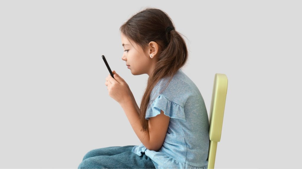 Girl sitting with forward head posture while using a phone, highlighting the need for child posture correction.