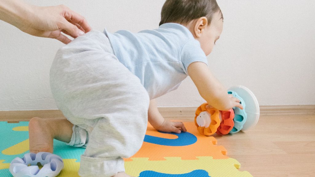Baby crawling on colourful play mat, reaching for toy during milestone observation