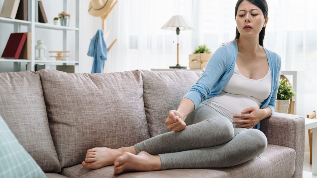 Pregnant woman resting on sofa, looking uncomfortable with wrist or leg pain