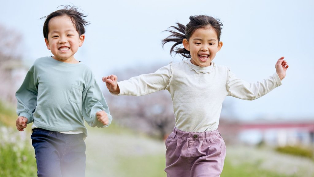Two happy children running outdoors, showing that mild intoeing does not stop kids from enjoying sports.