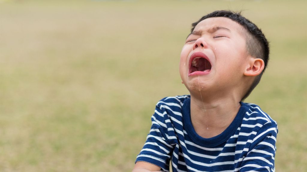 Young boy crying due to foot pain caused by plantar warts on the sole
