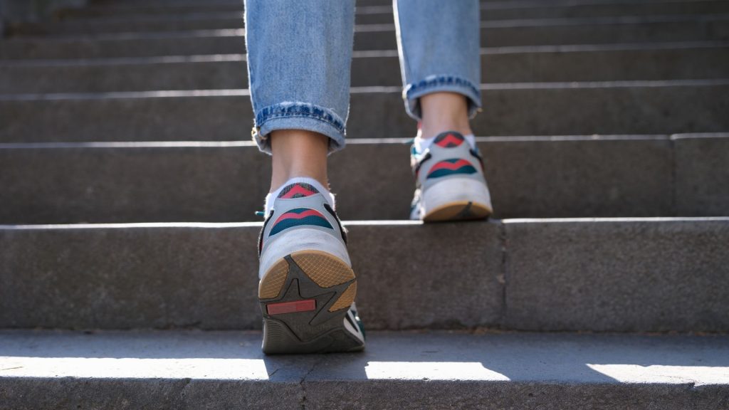Rear view of a woman walking up stairs in supportive sneakers, illustrating proper footwear for reducing foot and leg pain.