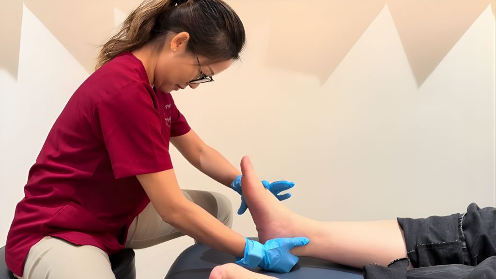 Clinician performing a hands-on foot mobility test on a patient lying on a treatment bed.