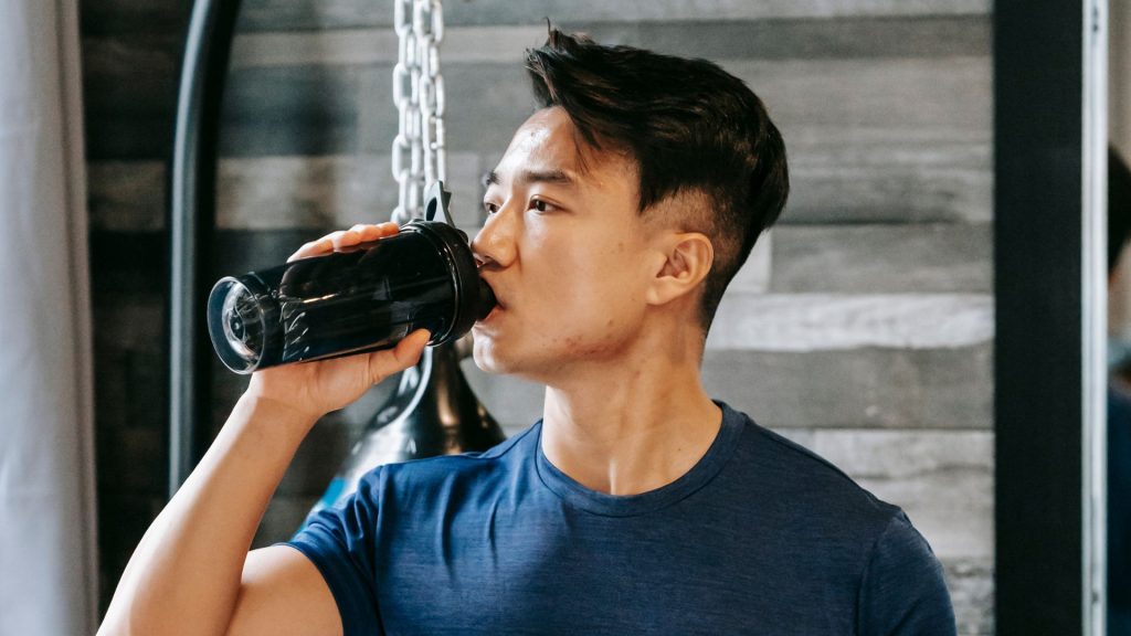 Young man drinking water after exercise, highlighting the role of hydration in bladder control and urinary health.