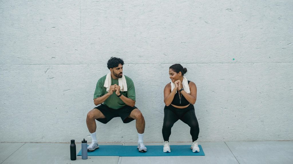 Man and woman performing squats together on yoga mats, showing exercises that help strengthen core and pelvic floor muscles.