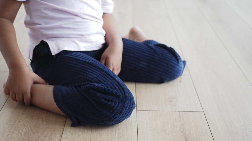 Child sitting in a W-position on the floor, illustrating common postural habits seen in children with joint hypermobility and reduced hip stability.