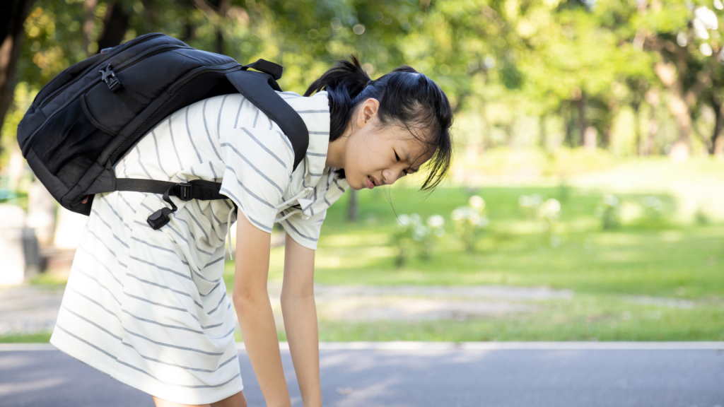 School-going child bending forward with a heavy backpack, illustrating fatigue and postural strain that can be more noticeable in children with joint hypermobility.