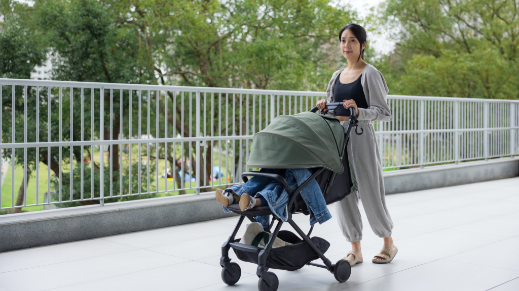 Mother walking outdoors while pushing a baby stroller, illustrating a common daily activity that may aggravate postpartum pelvic girdle or lower back pain.